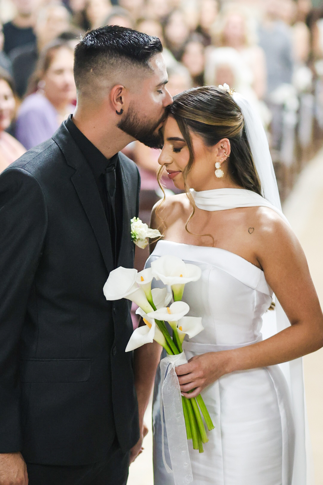 Noivo beijando a testa da noiva segurando buquê de copos-de-leite